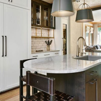 aspen colorado Elegant kitchen featuring a marble-topped island with dark wood base, leather bar stools, pendant lights, white cabinetry, and a subway tile backsplash.