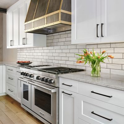 aspen Contemporary kitchen close-up with white cabinetry, gray subway tile backsplash, high-end stainless steel range, and a bouquet of fresh tulips on the marble countertop.